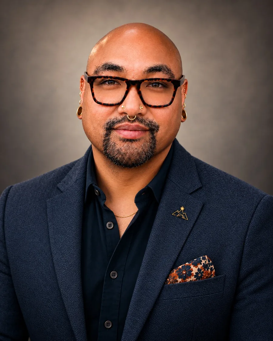 RJ Mabanta in a navy blazer and tortoiseshell glasses, with a gold pin on the lapel and a floral pocket square.